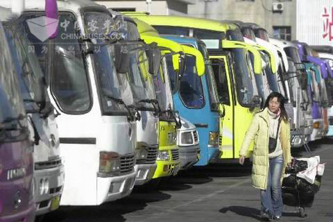 一位回家的旅客經過停靠在汽車站里整裝待發的大客車前